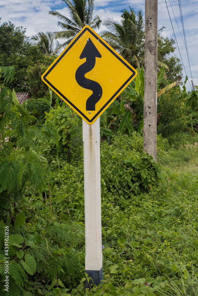 Road sign curved reminds the motorists and vehicles while driving with yellow sign reflecting light to be visible at night at the roadway in countryside of Thailand