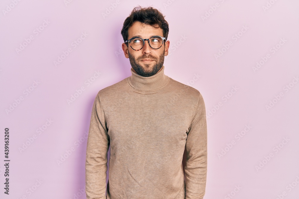 Handsome man with beard wearing turtleneck sweater and glasses smiling looking to the side and staring away thinking. Handsome man with beard wearing turtleneck sweater and glasses smiling looking to the side and staring away thinking.