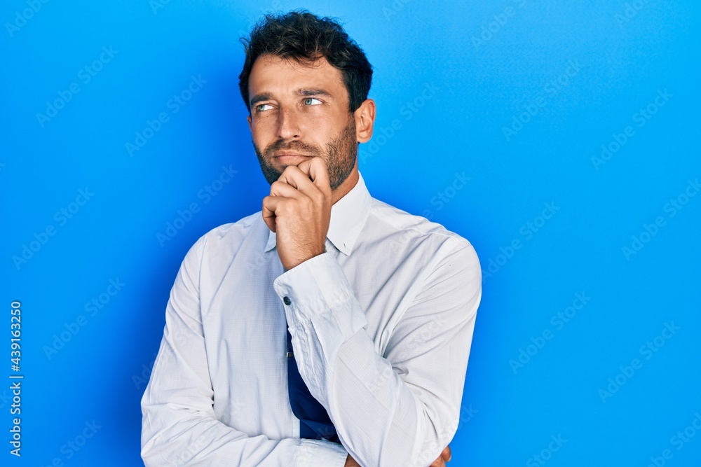 Handsome man with beard wearing business shirt and tie thinking concentrated about doubt with finger on chin and looking up wondering Handsome man with beard wearing business shirt and tie thinking concentrated about doubt with finger on chin and looking up wondering