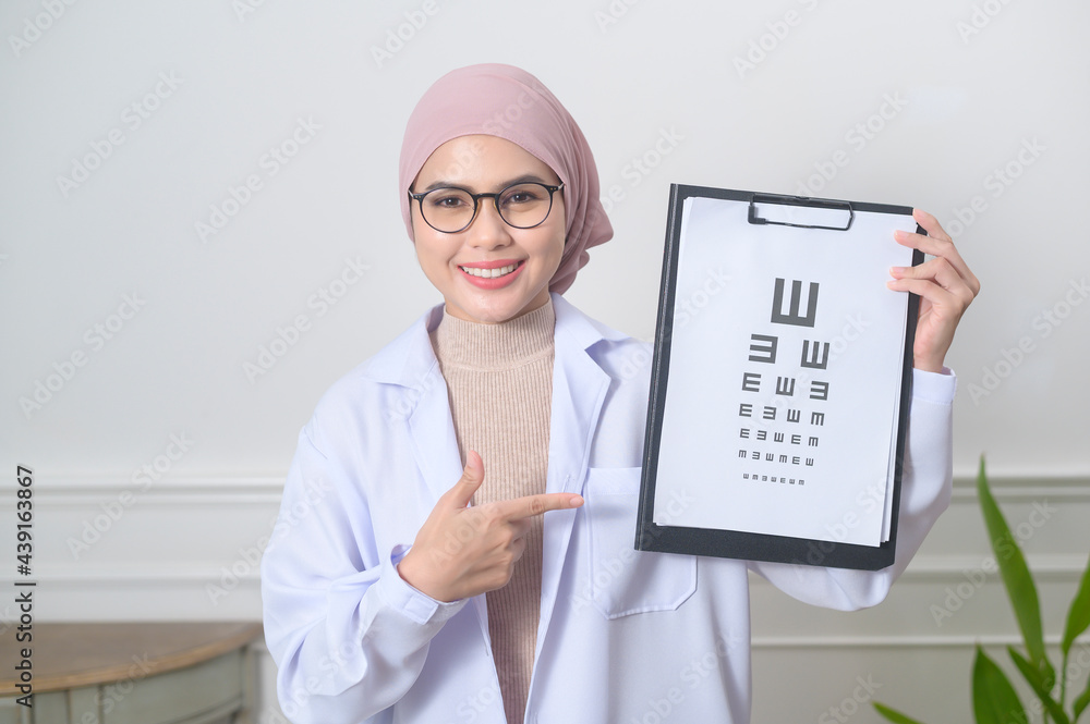 Female muslim ophthalmologist holding a vision chart test for measuring visual acuity Female muslim ophthalmologist holding a vision chart test for measuring visual acuity