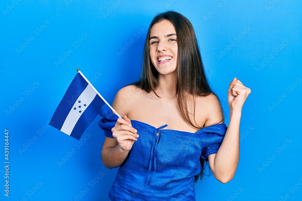 Young brunette teenager holding honduras flag screaming proud, celebrating victory and success very excited with raised arm Young brunette teenager holding honduras flag screaming proud, celebrating victory and success very excited with raised arm