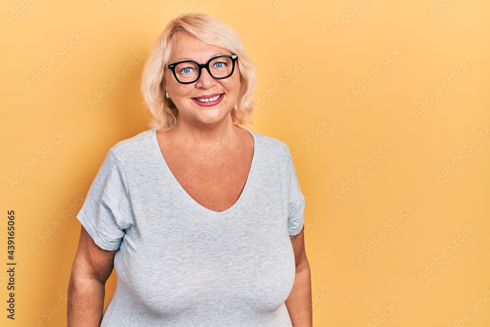 Middle age blonde woman wearing casual clothes and glasses looking positive and happy standing and smiling with a confident smile showing teeth Middle age blonde woman wearing casual clothes and glasses looking positive and happy standing and smiling with a confident smile showing teeth