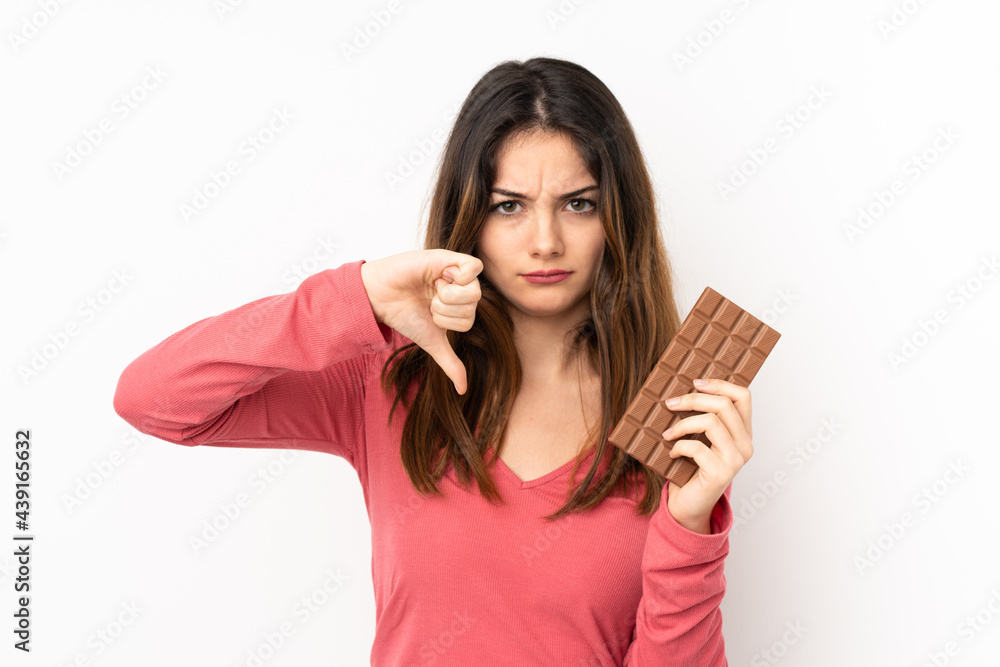 Young caucasian woman isolated on pink background taking a chocolate tablet making bad signal Young caucasian woman isolated on pink background taking a chocolate tablet making bad signal