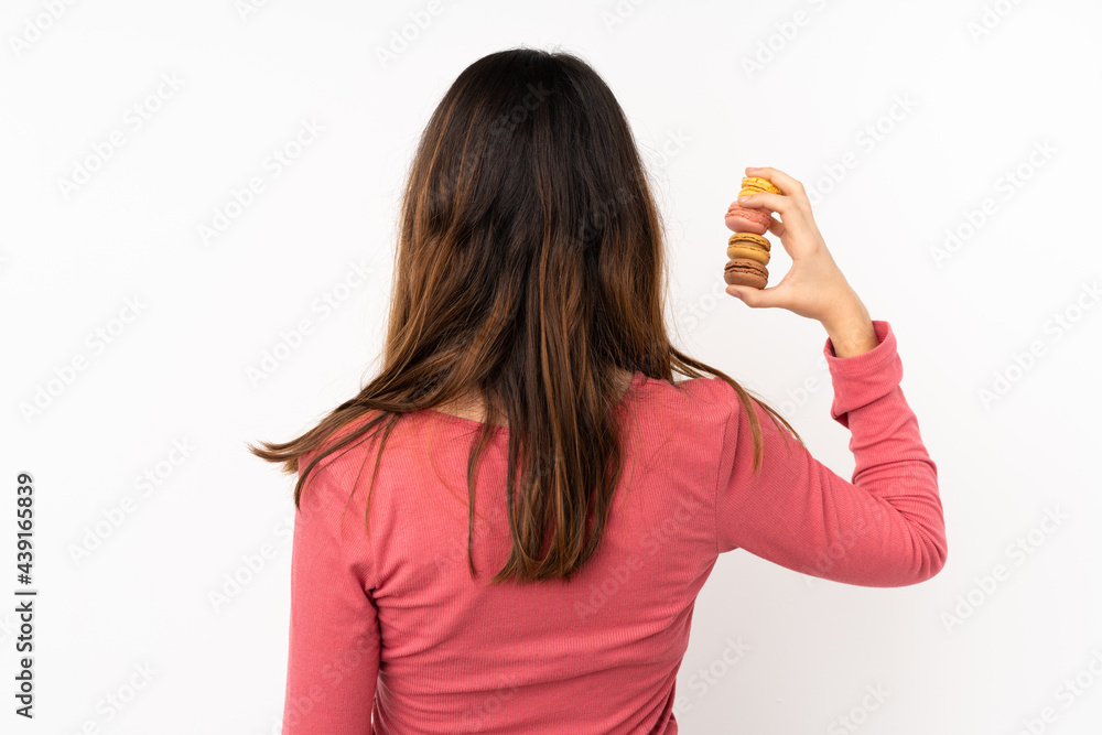 Young caucasian woman isolated on pink background holding colorful French macarons in back position Young caucasian woman isolated on pink background holding colorful French macarons in back position