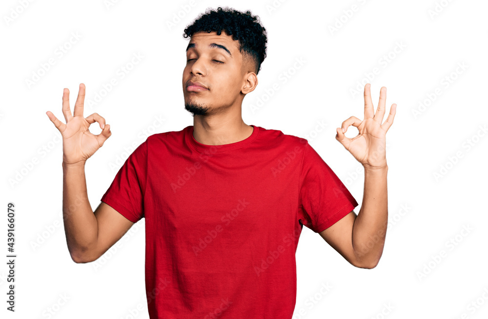 Young african american man wearing casual red t shirt relax and smiling with eyes closed doing meditation gesture with fingers. yoga concept. Young african american man wearing casual red t shirt relax and smiling with eyes closed doing meditation gesture with fingers. yoga concept.