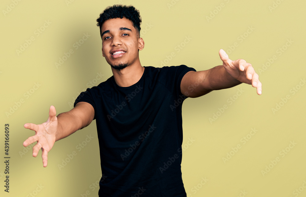 Young african american man wearing casual black t shirt looking at the camera smiling with open arms for hug. cheerful expression embracing happiness. Young african american man wearing casual black t shirt looking at the camera smiling with open arms for hug. cheerful expression embracing happiness.