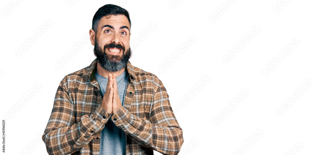 Hispanic man with beard wearing casual shirt begging and praying with hands together with hope expression on face very emotional and worried. begging. Hispanic man with beard wearing casual shirt begging and praying with hands together with hope expression on face very emotional and worried. begging.