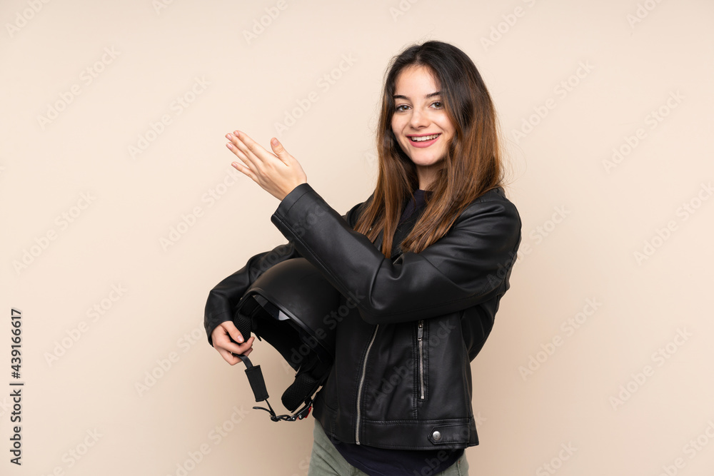 Woman with a motorcycle helmet isolated on beige background extending hands to the side for inviting to come Woman with a motorcycle helmet isolated on beige background extending hands to the side for inviting to come
