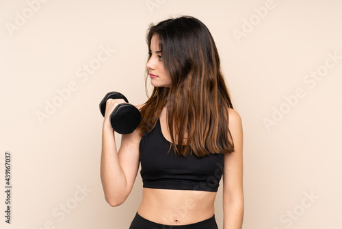 Young sport woman making weightlifting isolated on beige background looking side