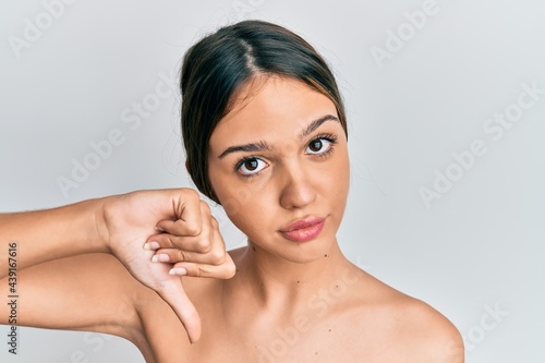 Young brunette woman standing topless showing skin with angry face, negative sign showing dislike with thumbs down, rejection concept