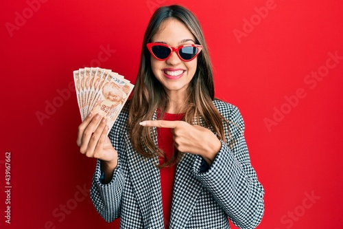 Young brunette woman holding 50 turkish lira banknotes smiling happy pointing with hand and finger photo