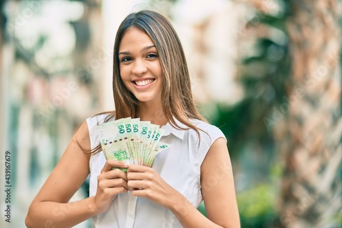 Beautiful latin teenager girl smiling happy holding hong kong dollars at the city.