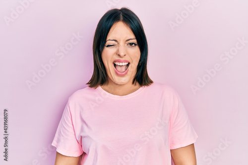 Young hispanic woman wearing casual pink t shirt winking looking at the camera with sexy expression, cheerful and happy face.