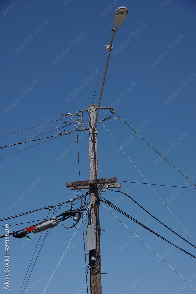 Low angle view of an electricity distribution pylon with a street light and power lines under blue sky
