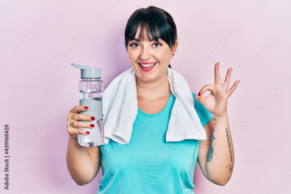 Young hispanic woman wearing sportswear holding water bottle doing ok sign with fingers, smiling friendly gesturing excellent symbol Young hispanic woman wearing sportswear holding water bottle doing ok sign with fingers, smiling friendly gesturing excellent symbol