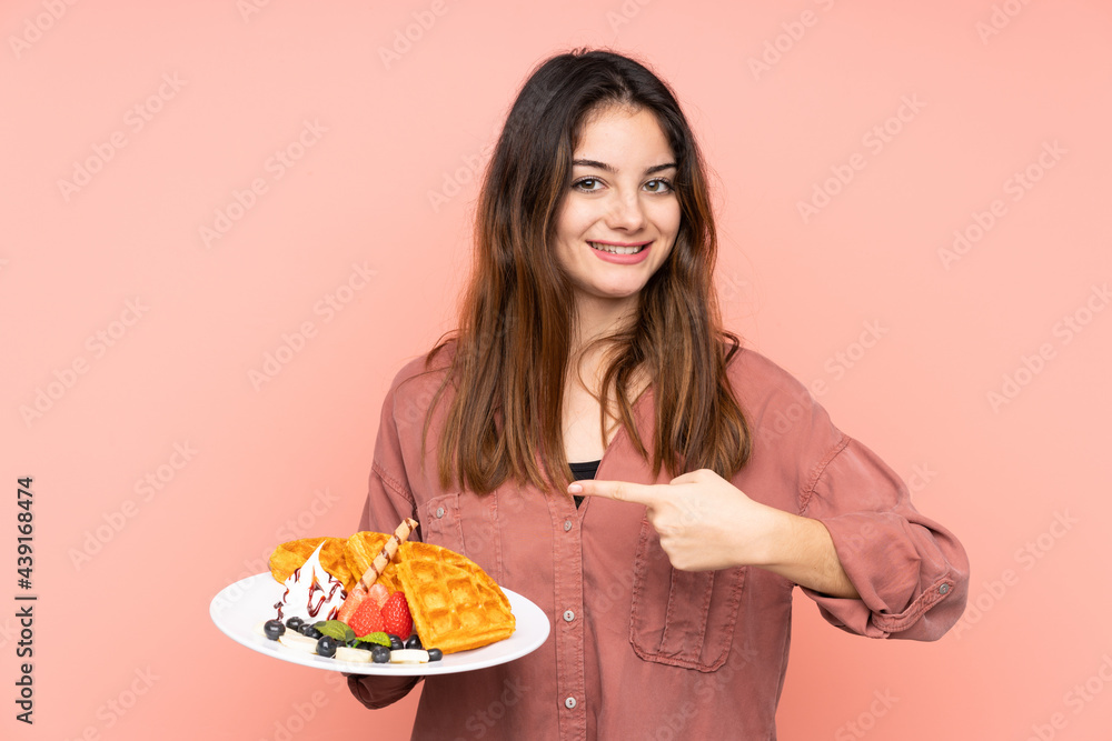 Young caucasian woman holding waffles isolated on pink background and pointing it Young caucasian woman holding waffles isolated on pink background and pointing it