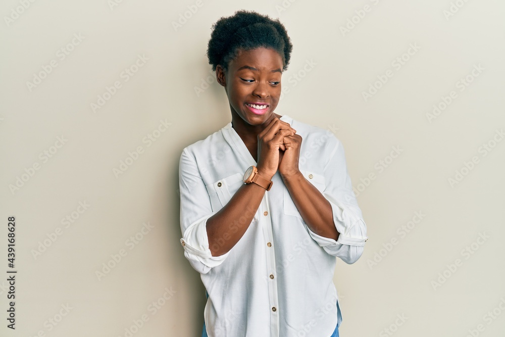 Young african american girl wearing casual clothes laughing nervous and excited with hands on chin looking to the side Young african american girl wearing casual clothes laughing nervous and excited with hands on chin looking to the side