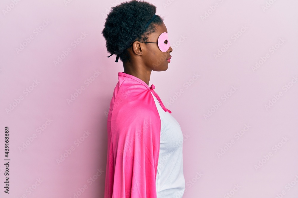 Young african american girl wearing superhero mask and cape costume looking to side, relax profile pose with natural face with confident smile. Young african american girl wearing superhero mask and cape costume looking to side, relax profile pose with natural face with confident smile.