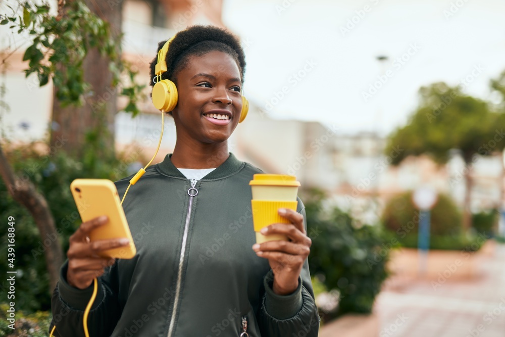 Fototapeta premium Young african american girl drinking coffee using smartphone and headphones at the city