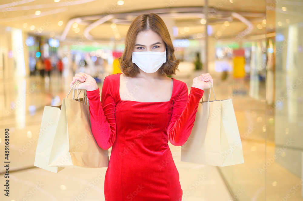 Young woman in red dress wearing protective mask in shopping mall, shopping under Covid-19 pandemic concept. Young woman in red dress wearing protective mask in shopping mall, shopping under Covid-19 pandemic concept.