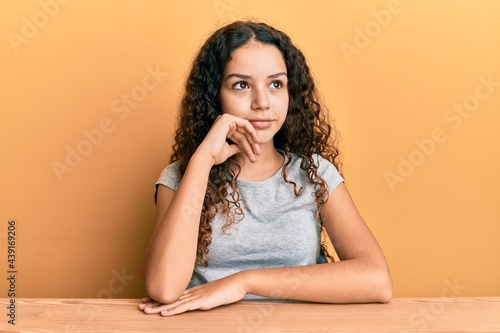 Teenager hispanic girl wearing casual clothes sitting on the table with hand on chin thinking about question, pensive expression. smiling and thoughtful face. doubt concept. © Krakenimages.com