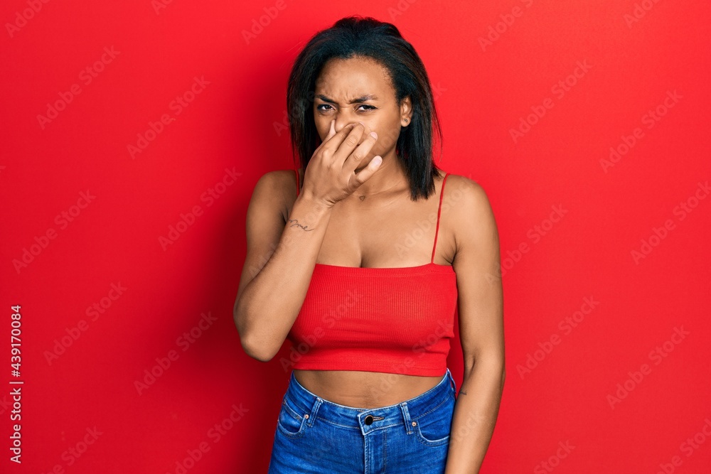 Young african american girl wearing casual style with sleeveless shirt smelling something stinky and disgusting, intolerable smell, holding breath with fingers on nose. bad smell Young african american girl wearing casual style with sleeveless shirt smelling something stinky and disgusting, intolerable smell, holding breath with fingers on nose. bad smell