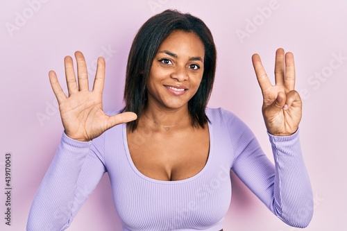 Young african american girl wearing casual clothes showing and pointing up with fingers number eight while smiling confident and happy. © Krakenimages.com