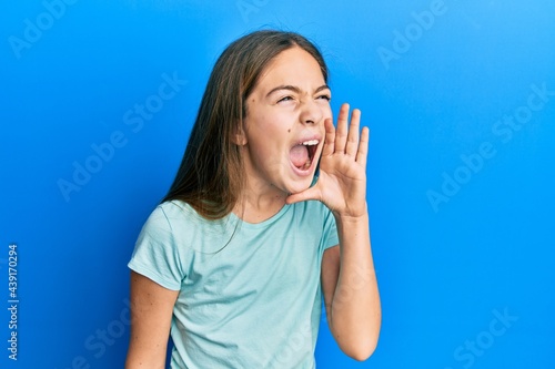 Beautiful brunette little girl wearing casual white t shirt shouting and screaming loud to side with hand on mouth. communication concept.
