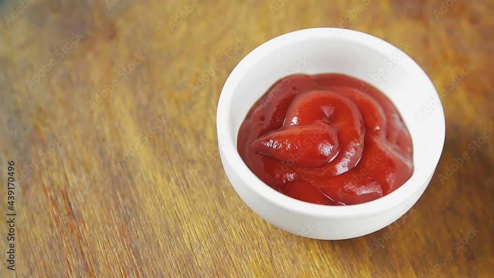 Tomato ketchup in a white gravy boat on a wooden background rotates in a circle. Tomato ketchup in a white gravy boat on a wooden background rotates in a circle.