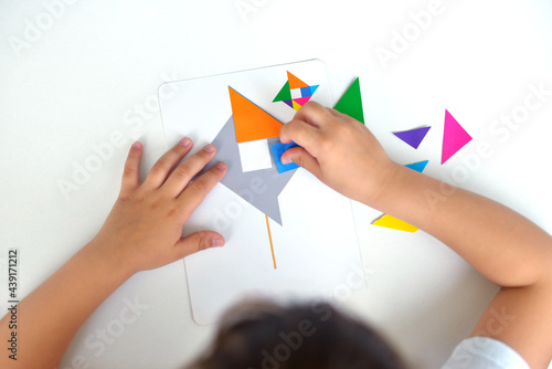 A preschooler girl sitting at the table collects a drawing from a geometric figure. the concept of early childhood development by montessori. a game of logic and imagination. photo
