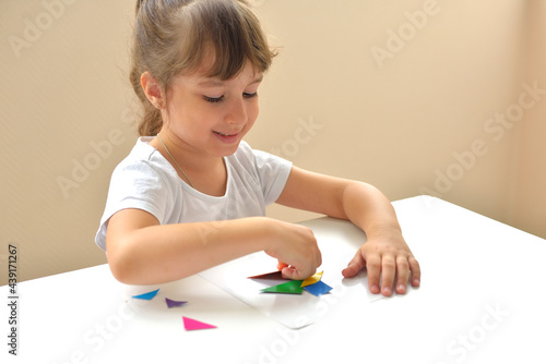 A preschooler girl sitting at the table collects a drawing from a geometric figure. the concept of early childhood development by montessori. a game of logic and imagination.