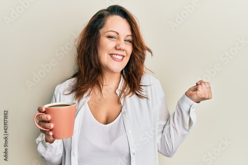 Young caucasian woman holding coffee screaming proud  celebrating victory and success very excited with raised arm