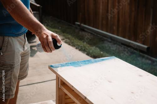 Hand of young man paints an unfinished table with blue spray paint