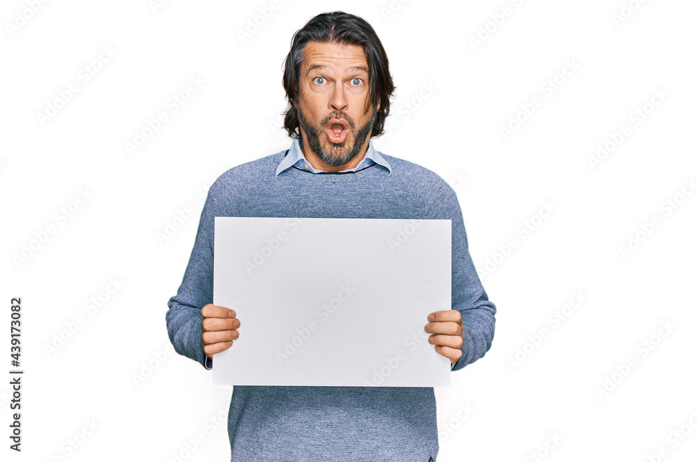 Middle age handsome man holding blank empty banner scared and amazed with open mouth for surprise, disbelief face Middle age handsome man holding blank empty banner scared and amazed with open mouth for surprise, disbelief face