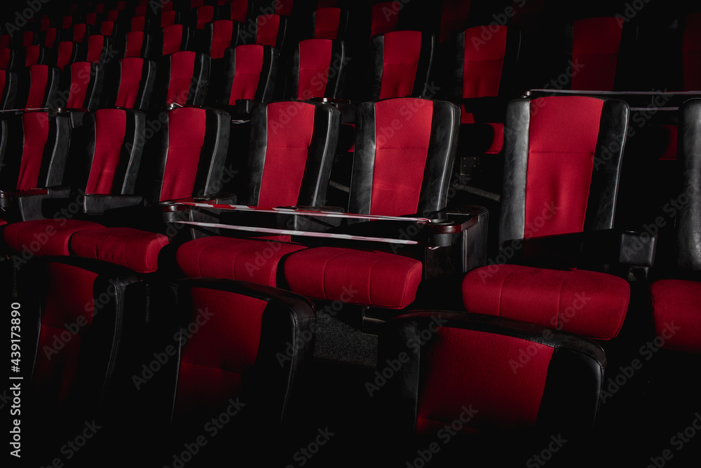 Obraz premium Empty movie theater. Armchairs red and black in the cinema hall are illuminated by a beam of light, low key. Selective focus. Quarantine, restrictive tape on chairs