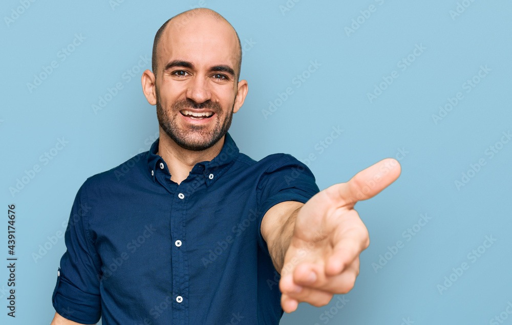 Naklejka premium Young hispanic man wearing casual clothes smiling friendly offering handshake as greeting and welcoming. successful business.