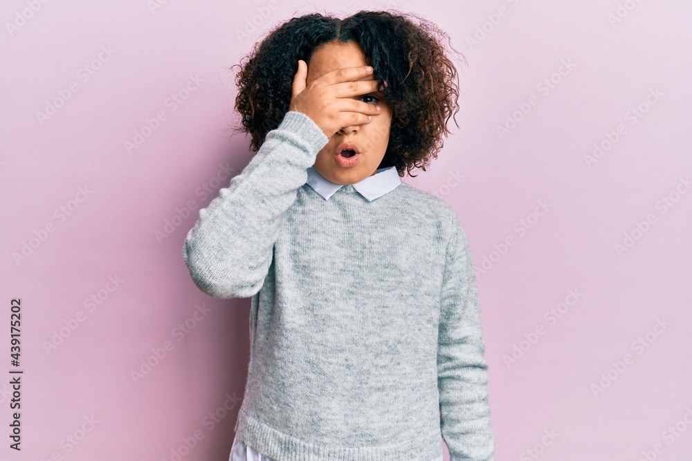 Young little girl with afro hair wearing casual clothes peeking in shock covering face and eyes with hand, looking through fingers afraid Young little girl with afro hair wearing casual clothes peeking in shock covering face and eyes with hand, looking through fingers afraid