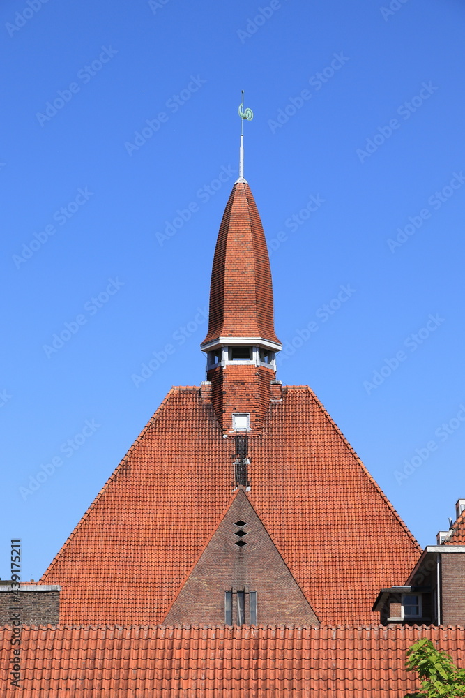 Obraz premium Amsterdam School of Architecture Building Detail with Spire and Red Roof Tiles Against a Blue Sky in Amsterdam, Baarsjes District