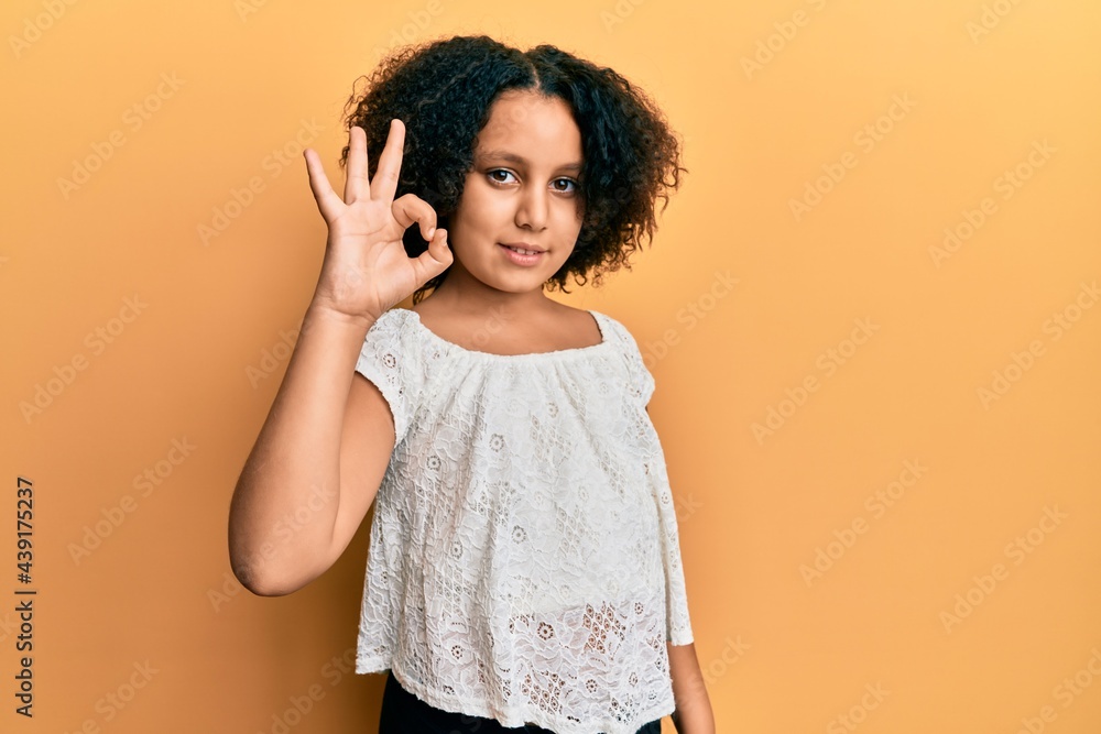 Young little girl with afro hair wearing casual clothes smiling positive doing ok sign with hand and fingers. successful expression. Young little girl with afro hair wearing casual clothes smiling positive doing ok sign with hand and fingers. successful expression.