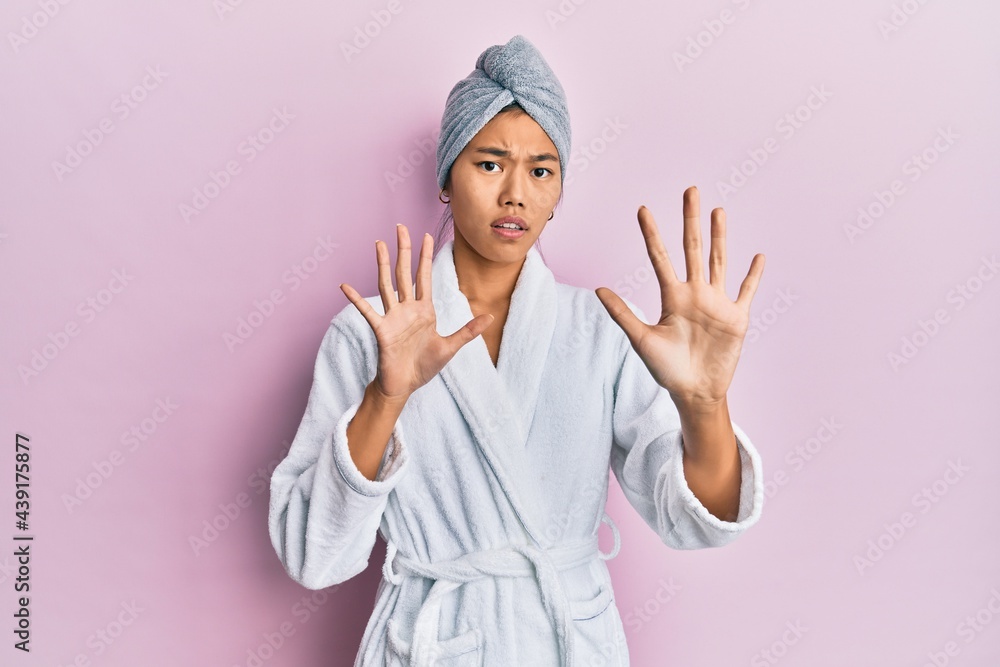 Young chinese woman wearing shower towel cap and bathrobe afraid and terrified with fear expression stop gesture with hands, shouting in shock. panic concept. Young chinese woman wearing shower towel cap and bathrobe afraid and terrified with fear expression stop gesture with hands, shouting in shock. panic concept.