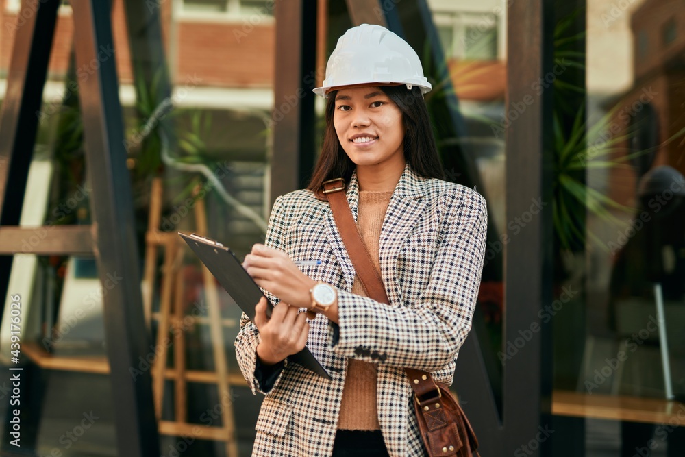 Young asian architect woman smiling happy writing on clipboard at the city. Young asian architect woman smiling happy writing on clipboard at the city.