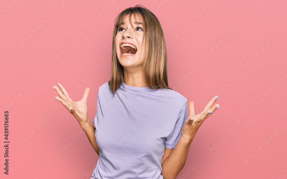 Teenager caucasian girl wearing casual clothes crazy and mad shouting and yelling with aggressive expression and arms raised. frustration concept. Teenager caucasian girl wearing casual clothes crazy and mad shouting and yelling with aggressive expression and arms raised. frustration concept.