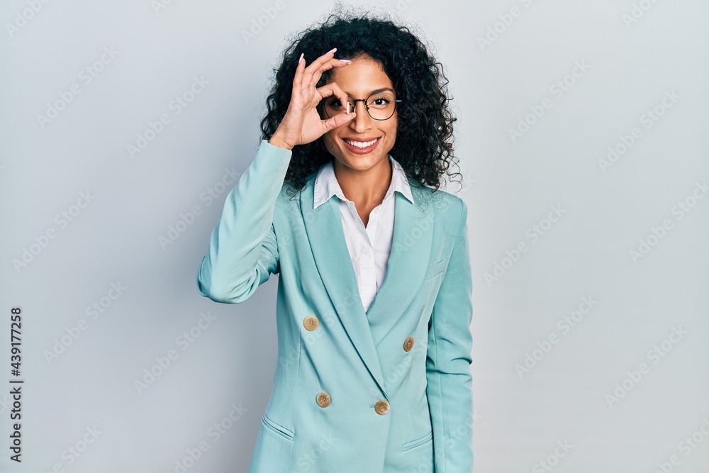 Young latin girl wearing business clothes and glasses doing ok gesture with hand smiling, eye looking through fingers with happy face.