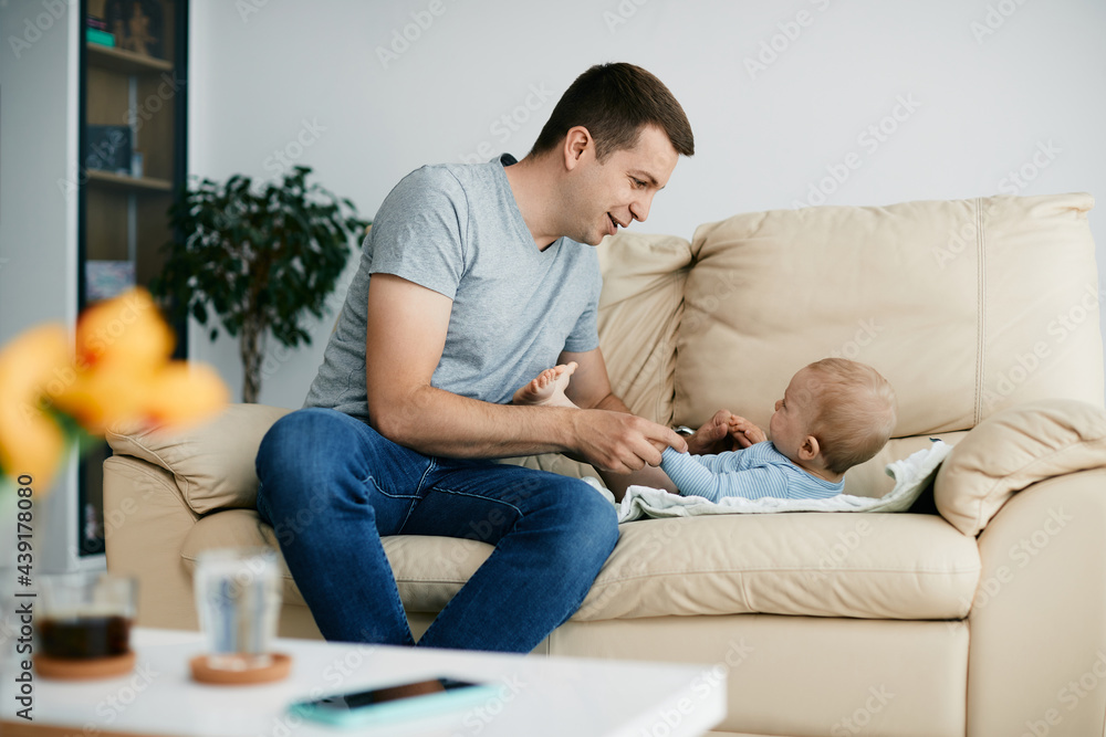 Young smiling father spending time with his baby son at home.