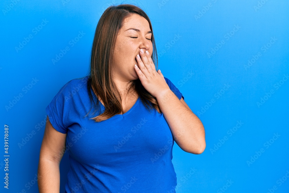 Beautiful brunette plus size woman wearing casual blue t shirt bored yawning tired covering mouth with hand. restless and sleepiness. Beautiful brunette plus size woman wearing casual blue t shirt bored yawning tired covering mouth with hand. restless and sleepiness.