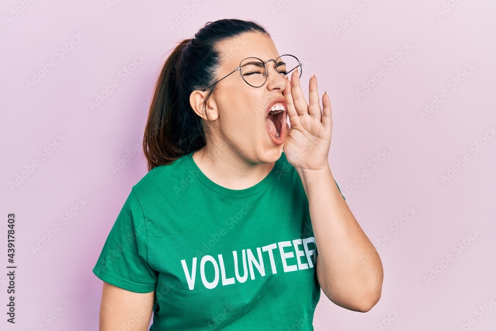 Young hispanic woman wearing volunteer t shirt shouting and screaming loud to side with hand on mouth. communication concept. Young hispanic woman wearing volunteer t shirt shouting and screaming loud to side with hand on mouth. communication concept.