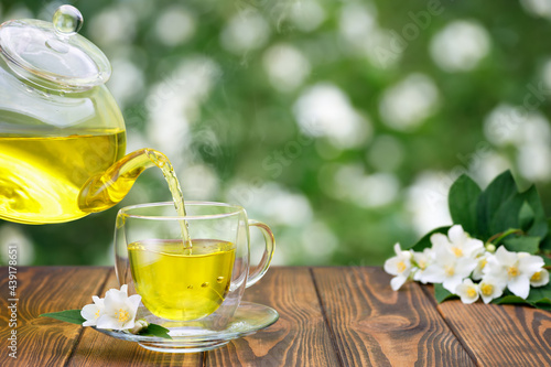 green tea with jasmine flowers pouring from glass teapot in cup