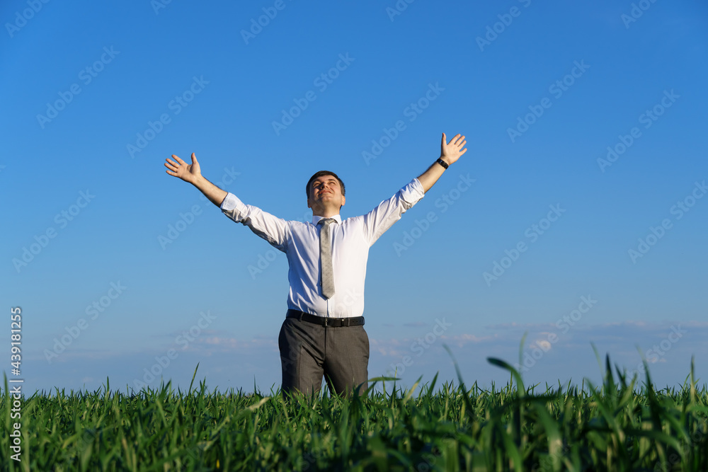 businessman poses in a field, he looks into the distance and rests, green grass and blue sky as background businessman poses in a field, he looks into the distance and rests, green grass and blue sky as background
