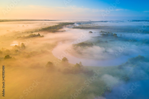 Misty morning river in sunlight. River landscape aerial view. Riverside view from above. Summer nature in sun rays. Drone view on sunny nature with curved river. Scenery river top view.