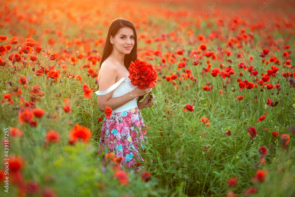 A beautiful brunette with a red bouquet in the poppy field at sunset A beautiful brunette with a red bouquet in the poppy field at sunset